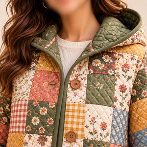K&ouml;nnte beinhalten: Eine gesteppte Kapuzenjacke mit einem Patchwork-Design aus verschiedenen Blumen- und Vichy-Karomustern in Olivgr&uuml;n, Senfgelb, Altrosa und Blau. Die Jacke hat einen einfarbigen olivgr&uuml;nen Saum und zwei runde braune Kn&ouml;pfe.
