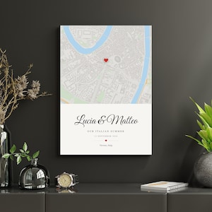 Puede incluir: Una impresión de arte mural rectangular que muestra un mapa de ciudad en tonos claros con un pequeño icono de corazón rojo. Debajo del mapa, el texto dice Lucia & Matteo, OUR ITALIAN SUMMER, 12 SEPTEMBER 2020 y Verona, Italy, con un corazón.