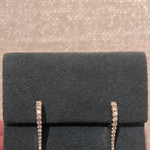 May include: A pair of diamond earrings with a curved design. The earrings are on a gray velvet background.