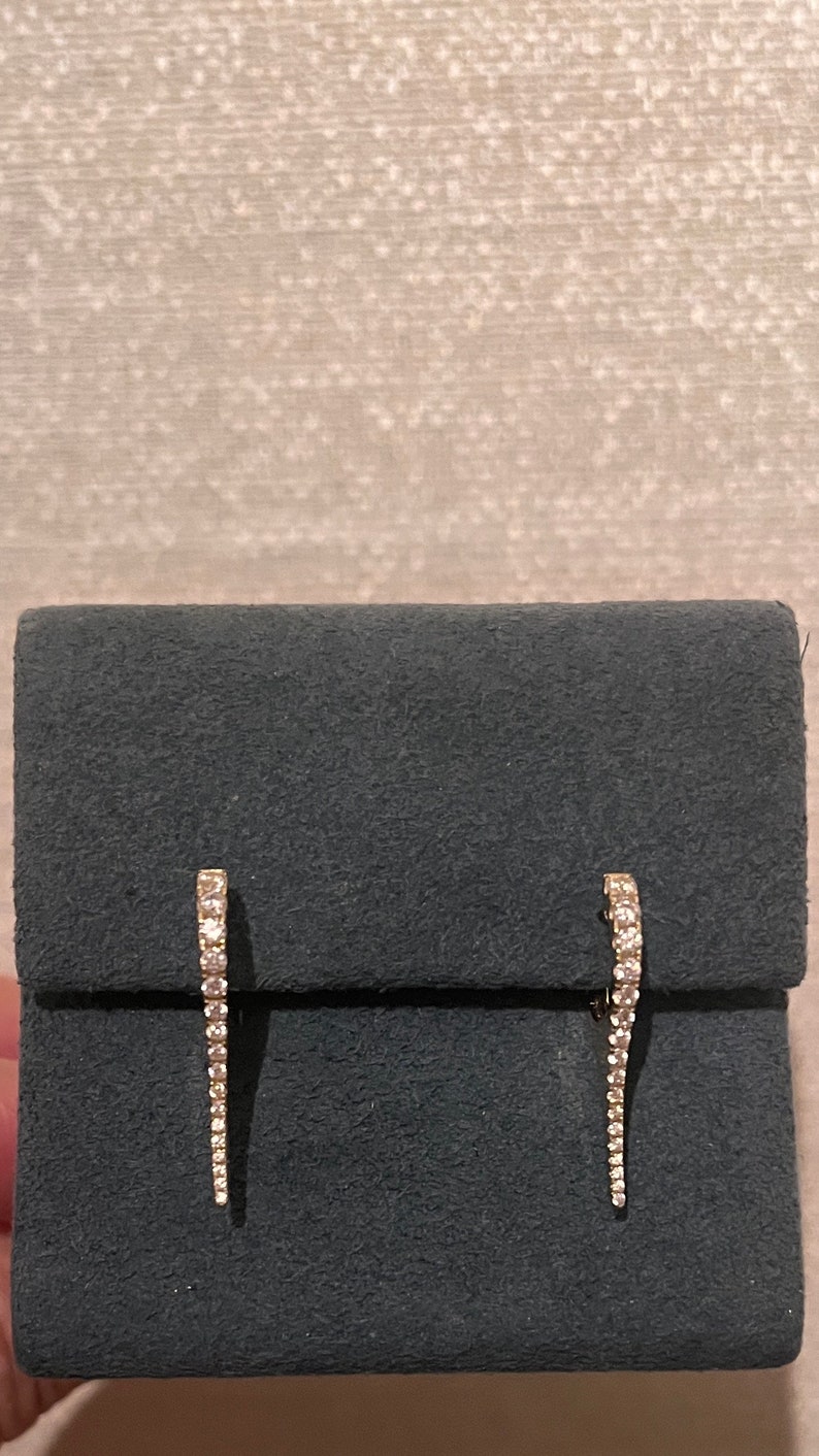May include: A pair of diamond earrings with a curved design. The earrings are on a gray velvet background.