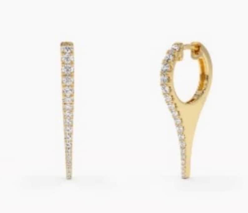 May include: A pair of gold hoop earrings with a pointed tip. The hoops are set with small, clear diamonds.