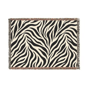 May include: A rectangular woven throw blanket featuring a high-contrast black and off-white zebra stripe pattern. The edges of the blanket are finished with a decorative fringe detail that incorporates subtle multi-colored threads throughout.