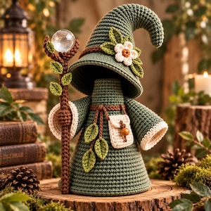 Peut inclure: Une figurine en crochet représentant un personnage portant un chapeau pointu vert orné d'une fleur blanche et de feuilles vertes. Le personnage porte une robe verte avec une ceinture marron, une petite pochette crème et tient un bâton marron.