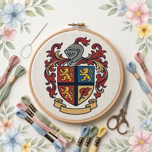 May include: A circular wooden embroidery hoop containing a cross-stitched coat of arms featuring a silver helmet, red and gold mantling, and a shield divided into four quadrants with lions and a leaf, surrounded by embroidery floss and scissors.