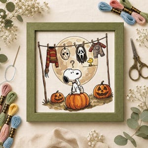 May include: A framed cross-stitch embroidery featuring Snoopy sitting on a pumpkin under a full moon. A clothesline hangs above with a striped jumper, a hockey mask, a ghost mask, and dungarees. Woodstock sits nearby, and two jack-o'-lanterns sit on the ground.
