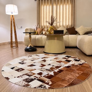 May include: A circular area rug featuring a patchwork design of cowhide squares in various shades of brown, white, and black. The rug is composed of numerous small, stitched-together pieces, creating a textured, multi-toned pattern on the floor.
