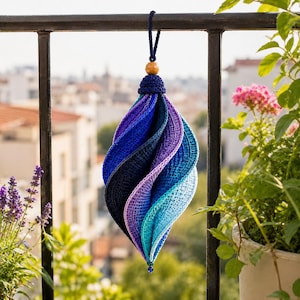 May include: A spiral-shaped crochet ornament featuring a gradient of blue and purple yarn colors. The ornament is suspended by a dark blue cord topped with a single wooden bead and finished with a small dark blue bead at the bottom point.