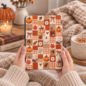 May include: A rectangular e-reader case featuring a patchwork design of orange, brown, and cream squares. The pattern includes illustrations of pumpkins, acorns, autumn leaves, daisies, bows, and mugs of hot cocoa on books in a seasonal theme.