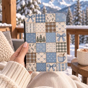 May include: A rectangular e-reader case featuring a patchwork design of light blue, white, and brown squares. The pattern includes illustrations of bows, snowflakes, pine trees, hearts, floral sprigs, plaid, and a mug of hot cocoa with whipped cream.