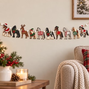 May include: A decorative garland featuring ten individual wooden horse ornaments strung together with small white pom-poms. Each horse is illustrated in a unique holiday-themed outfit, including Santa hats, festive sweaters, scarves, and wreaths.