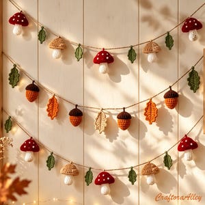 Op de afbeelding: Een decoratieve slinger met gehaakte rood-witte paddenstoelen, bruine eikels en groene en oranje bladeren aan een dun touw. De items zijn gerangschikt in drie horizontale rijen en tonen gedetailleerde garentexturen en herfstkleuren.