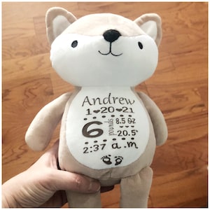 May include: A plush fox stuffed animal with a white belly and brown fur. The belly is embroidered with the name "Andrew", the date "1-20-21", the weight "6 pounds 8.5 oz", the length "20.5"
