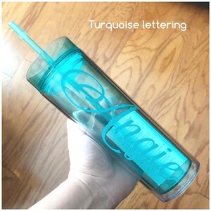 May include: A clear, reusable tumbler with a turquoise lid and straw. The tumbler has a turquoise inscription that reads "Laurie" in a cursive font.