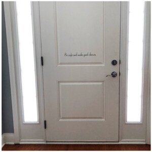 May include: White door with a glass panel on each side. The door has a black door handle and a black door knob. The words "Be safe and make good choices" are written in black cursive on the door.