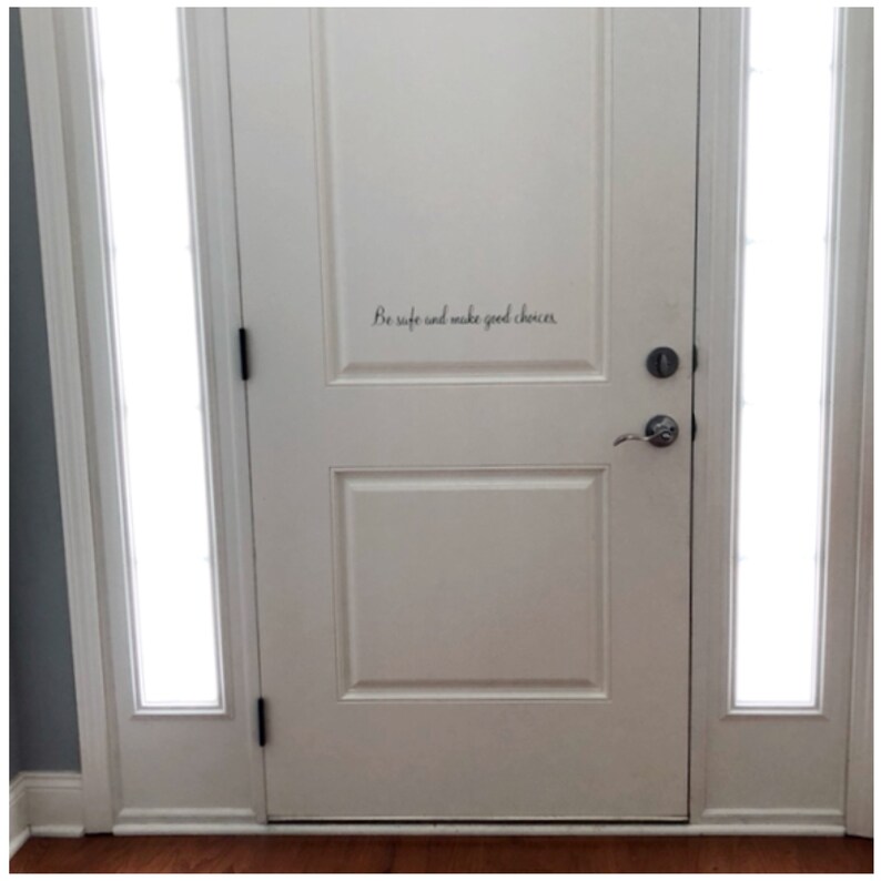 May include: White door with a glass panel on each side. The door has a black door handle and a black door knob. The words "Be safe and make good choices" are written in black cursive on the door.