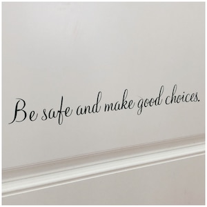 May include: White wall with black cursive text that reads "Be safe and make good choices."