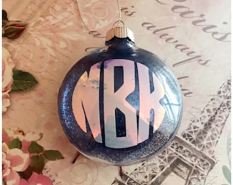 May include: A round, dark blue Christmas ornament with glitter and a silver cap. The ornament features the white letters "MRK" in a monogram design. A silver string is attached for hanging.