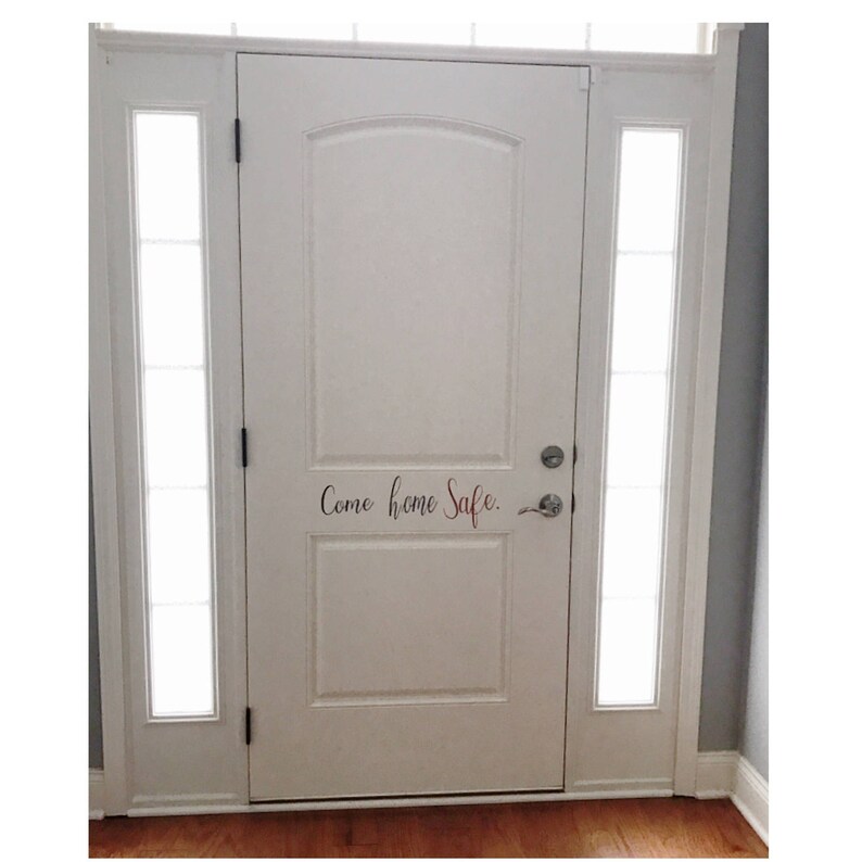 May include: White front door with a glass sidelight on each side. The door has a black handle and a silver door knob. The words "Come home Safe." are written in black cursive on the door.