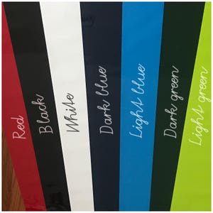 May include: A close-up of six different colored fabric swatches. The swatches are arranged from left to right: red, black, white, dark blue, light blue, dark green, and light green.
