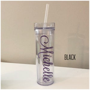 K&ouml;nnte beinhalten: Ein durchsichtiger Plastikbecher mit schwarzem Deckel und einem violetten Vinyl-Aufkleber mit der Aufschrift "Michelle". Der Becher hat einen Strohhalm und steht auf einer wei&szlig;en Oberfl&auml;che.