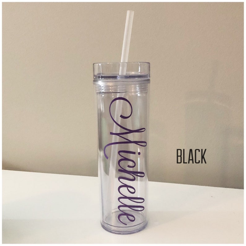 K&ouml;nnte beinhalten: Ein durchsichtiger Plastikbecher mit schwarzem Deckel und einem violetten Vinyl-Aufkleber mit der Aufschrift "Michelle". Der Becher hat einen Strohhalm und steht auf einer wei&szlig;en Oberfl&auml;che.