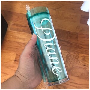 May include: A turquoise reusable tumbler with a clear lid and a white straw. The tumbler has the name "Diane" written on it in a cursive font.