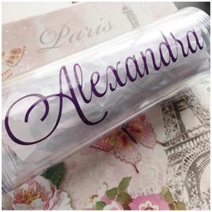 K&ouml;nnte beinhalten: Ein durchsichtiger Plastikbecher mit einem violetten Vinyl-Aufkleber, auf dem "Alexandra" steht.