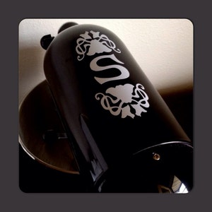 Puede incluir: Electrodoméstico de cocina negro con una calcomanía de vinilo blanco de una letra estilizada "S" y un diseño floral.