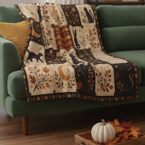 Può includere: Una coperta con design patchwork caratterizzata da sagome di gatti neri, lune crescenti, foglie autunnali, zucche e motivi scozzesi in tonalità crema, arancione, marrone e nero. La coperta presenta una disposizione a griglia con bordi decorativi.