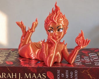 May include: A glossy orange and red 3D-printed figurine of a character with flame-like hair, resting on a book titled House of Earth and Blood by Sarah J. Maas. The figure has a pointed flame hairstyle, large eyes, and holds a small flame in one hand.