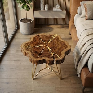 May include: A round coffee table featuring a natural wood slab top with a live edge and prominent wood grain. The surface is split by deep fissures filled with a metallic gold inlay. The table is supported by thin, angular gold metal legs.