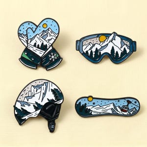 May include: A set of four enamel pins featuring winter sports gear: a pair of mittens, ski goggles, a helmet, and a snowboard. Each item displays a snowy mountain landscape with white peaks, dark green pine trees, a yellow sun, and a light blue sky.