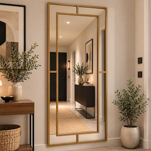 May include: A tall rectangular wall mirror featuring a thin gold metal frame with an internal geometric design that creates a smaller centered rectangular mirror section. The frame has clean lines and a smooth metallic finish, reflecting the interior space.