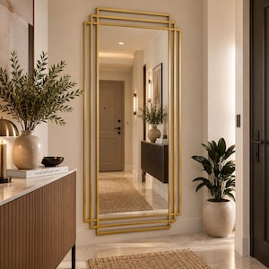 May include: A tall, rectangular wall mirror featuring a layered, geometric gold metal frame. The design consists of multiple overlapping rectangular outlines that create a structured, multi-dimensional appearance. The mirror surface is clear and reflective.
