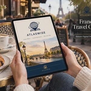 May include: A digital tablet displaying a France Travel Guide by Atlaswise. The cover features a globe and book logo, the text Iconic Places, Local Experiences, Practical Tips, and a photograph of the Eiffel Tower at sunset over the Seine river.