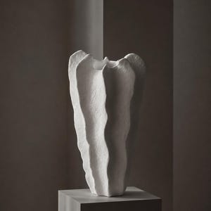 May include: A tall, white vase with a textured, matte surface and a distinctively organic, undulating vertical form. The vessel features deep, rhythmic ridges that create a series of wave-like folds along its exterior, culminating in a flared rim.