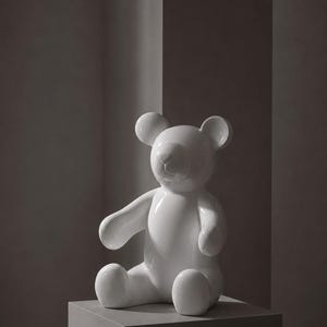 Op de afbeelding: Een glanzend wit keramieken teddybeerbeeldje in zittende positie. Het beeldhouwwerk heeft een glad, reflecterend oppervlak met ronde oren, een gedefinieerde snuit en uitgestrekte armen, wat een klassiek berensilhouet in een effen witte afwerking weergeeft.