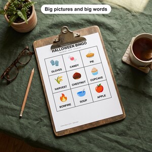May include: A Halloween Bingo game sheet on a wooden clipboard featuring a 3x3 grid with illustrations and labels for gloves, candy, pie, harvest, chestnut, cupcake, bonfire, soup, and apple. The text reads Big pictures and big words.