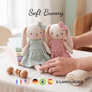 Könnte beinhalten: Zwei Plüschhasen-Puppen mit langen Ohren und gestickten Gesichtszügen. Ein Hase trägt ein hellgrünes Kleid mit einer kleinen Schleife, der andere ein rosa gepunktetes Kleid mit passender Schleife. Der Text Soft Bunny ist oben zu sehen.
