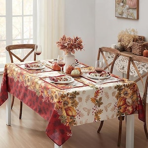 May include: A rectangular tablecloth featuring a print of pumpkins, sunflowers, and autumn leaves in shades of red, orange, and cream. The design includes a deep red border with a leaf pattern and a central cream section with seasonal motifs.