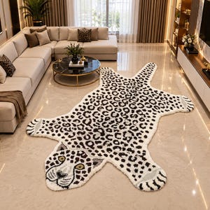 May include: A large, shaped area rug featuring a white background with a black and brown leopard print pattern. The rug is designed in the silhouette of a leopard, complete with a detailed head, four paws, and a tail, laid flat on the floor.