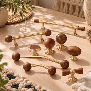 Puede incluir: Una colección de herrajes para muebles que combina metal dorado cepillado y madera de color marrón oscuro. El conjunto incluye varios tiradores de cajón con extremos de madera esféricos o cilíndricos y varios pomos de madera redondos u ovalados.