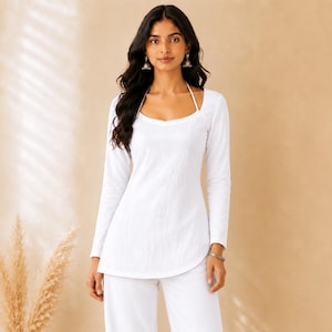 May include: A solid white long-sleeve top with a scoop neckline and thin halter straps paired with matching white wide-leg trousers. The ensemble features a clean, monochromatic design with a curved hemline on the top and a relaxed fit throughout.