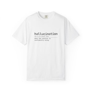 May include: A white short-sleeved t-shirt featuring black text printed on the chest. The text displays the word hallucination, its phonetic pronunciation, and the definition: when the machine is confidently wrong. The shirt has a crew neckline.