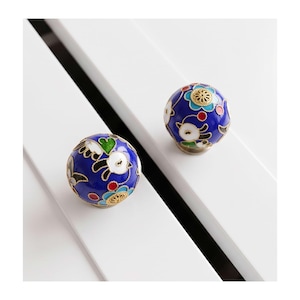May include: Two round cabinet knobs featuring a deep blue enamel base with intricate gold-toned metal filigree outlines. The surface is decorated with colorful floral patterns in shades of white, light blue, green, and red, creating a detailed design.