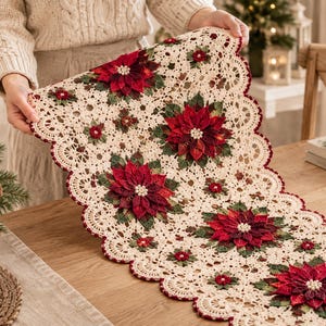 May include: A cream-colored crocheted table runner featuring a scalloped edge trimmed in dark red. The runner is decorated with multiple three-dimensional poinsettia flower motifs in shades of red and green, accented with small white beads.