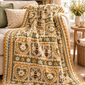 May include: A crochet blanket featuring a repeating pattern of squares with white daisy flowers, yellow and black bees, and heart-shaped motifs in shades of sage green, cream, and mustard yellow, finished with a scalloped yellow border edge.