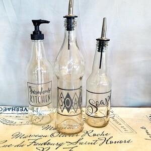 May include: Three glass bottles with black labels and black pump tops. The labels read "Farmhouse Kitchen", "Soap", and "Soap".