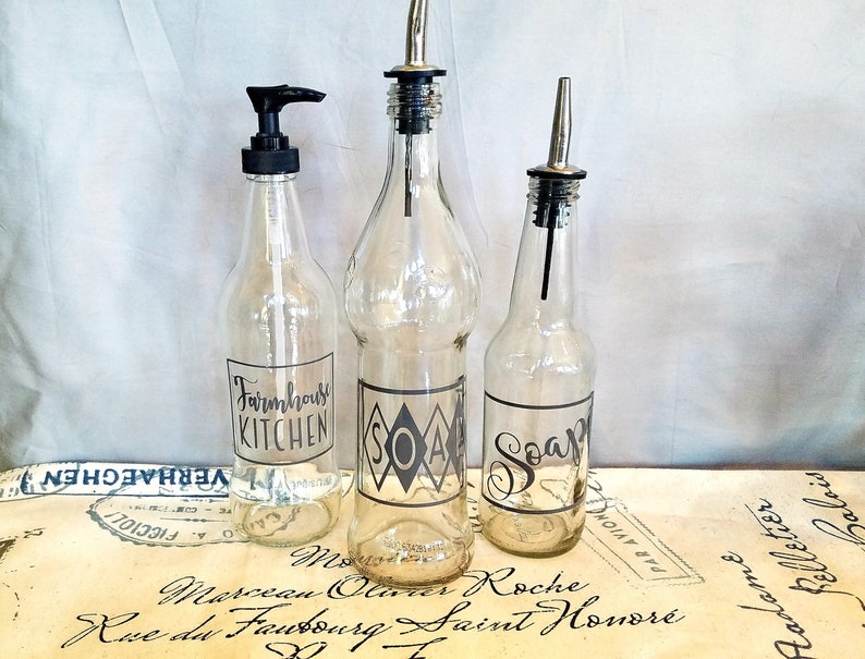 May include: Three glass bottles with black labels and black pump tops. The labels read "Farmhouse Kitchen", "Soap", and "Soap".