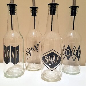 May include: Four clear glass bottles with black pump tops and black vinyl labels that say "SOAP" in different styles.